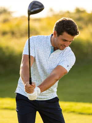 Outdoor shot of a model swinging a golf club, wearing the white blue florals stretch printed collarless henley golf shirts with a relaxed fit