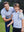 Father resting hand on son's shoulder on golf course, both wearing youth performance golf polos in white/light blue stripe