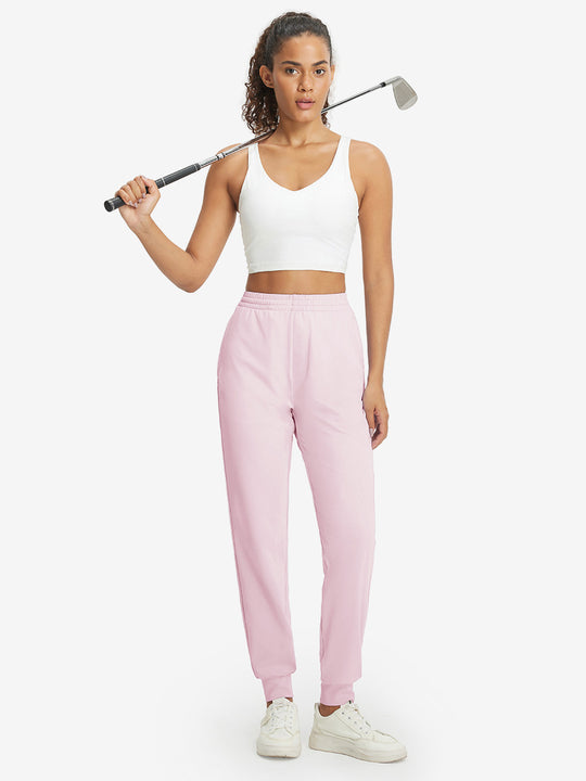 Model holding golf club behind neck while wearing lightweight women's stretchy joggers sweatpants in light purple.