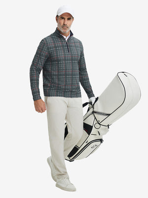 Full-body shot of model holding golf bag, dressed in full print quarter zip pullover in retro black/red plaid.