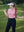 Model in pink women's performance solid polo holding a golf club outdoors
